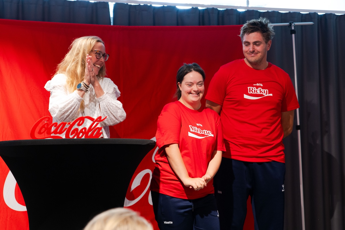 Två glada idrottare som också är ambassadörer för Special Olympics står på scenen i röda Coca-Cola tröjor.