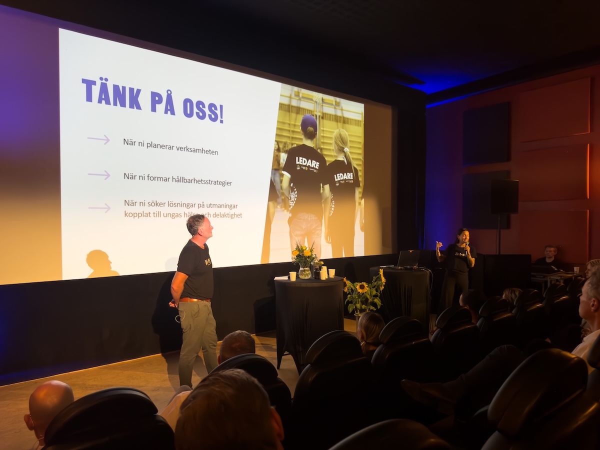 Jasmine Hanab Björnberg och Ted Åhs står framför en presentation som säger "Tänk på oss".